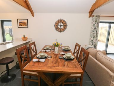 A dining table set for six with plates glasses and a vase of flowers in a room with wooden beams at The Byre in St Brides Major