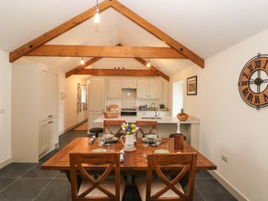 A dining area with a wooden table set for four and an open kitchen with exposed wooden beams at The Byre in St Brides Major