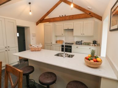 A kitchen with a white island countertop with sink stools and wooden beams at The Byre in St Brides Major