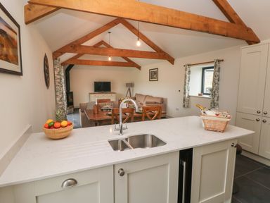 An open plan kitchen and living area with a kitchen island a dining table and a sofa at The Byre in St Brides Major