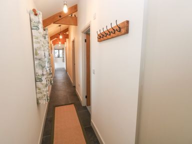 A hallway with wooden beams on the ceiling a row of hooks on the wall a window with patterned curtains and a floor rug at The Byre in St Brides Major