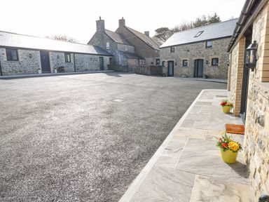 An outdoor paved area with stone buildings and flower pots at The Byre in St Brides Major