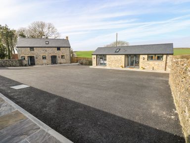 A courtyard with two stone buildings and asphalt ground at The Byre in St Brides Major