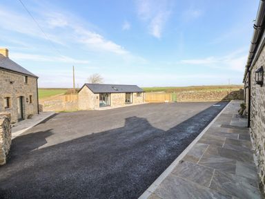 An outdoor area with stone buildings and paved walkway surrounded by fields at The Byre in St Brides Major