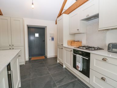 A kitchen with gray tiled floor white cabinets and a dark gray door at The Byre in St Brides Major