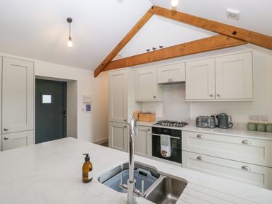A kitchen with a marble countertop island and sink cabinets oven toaster and kettle under wooden ceiling beams at The Byre in St Brides Major