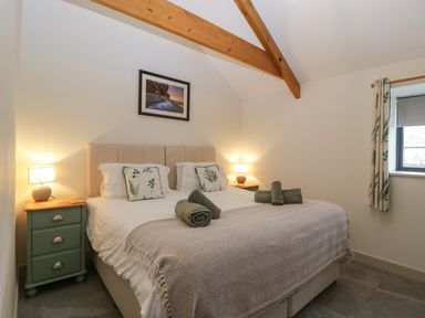 A bedroom with a double bed green bedside tables lamps a window and wooden ceiling beams at The Byre in St Brides Major