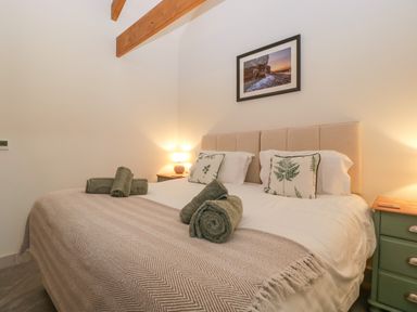 A bedroom with a double bed with rolled towels on it bedside tables with lamps and a framed picture on the wall at The Byre in St Brides Major