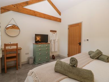 A bedroom with a bed and rolled towels a wooden chair a green chest of drawers and a TV at The Byre in St Brides Major