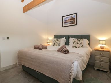 A bedroom with a double bed two bedside tables with lamps a framed picture above the bed and towels on the bed at The Byre in St Brides Major