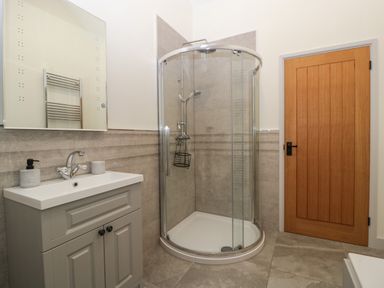 A bathroom with a shower enclosure a sink with cabinet a mirror and a wooden door at The Byre in St Brides Major