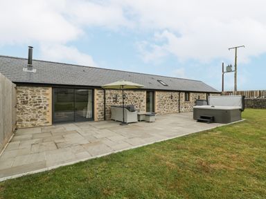 An outdoor patio area with stone flooring a hot tub seating with umbrella and a stone building at The Byre in St Brides Major