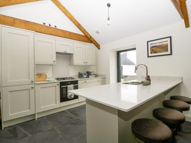 A kitchen with a countertop island and stools under wooden ceiling beams at The Byre in St Brides Major