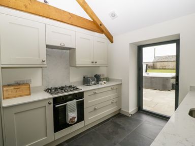 A kitchen with gray cabinets a gas stove an oven and a glass door leading outside at The Byre in St Brides Major