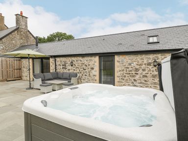 An outdoor patio with a hot tub a sofa set with an umbrella and stone building at The Byre in St Brides Major
