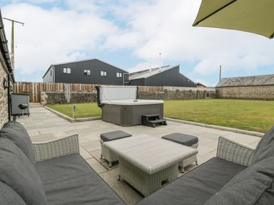 An outdoor patio with wicker furniture, a hot tub, lawn, and stone walls at The Byre in St Brides Major