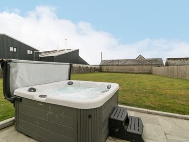 An outdoor hot tub with steps on a paved area next to a lawn with stone and wooden fences at The Byre in St Brides Major