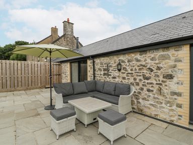 An outdoor patio with a wicker sectional sofa a table two stools and a large umbrella at The Byre in St Brides Major