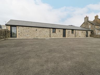 A single story stone building with black doors and windows and a large paved area in front at The Byre in St Brides Major
