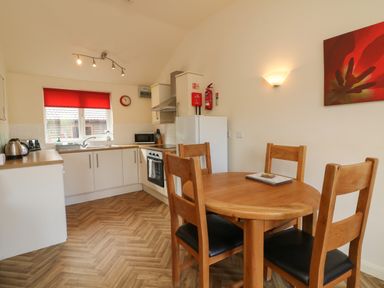 A kitchen with wooden dining table and chairs a fridge oven and a window with red blind at Chalet Log Cabin L2 in Combe Martin