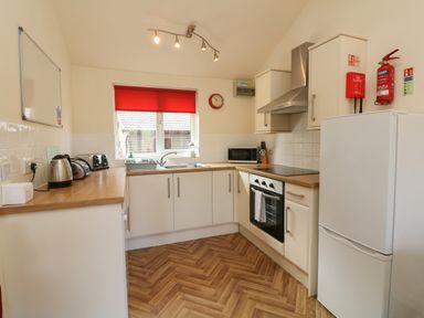 A kitchen with white cabinets wooden countertops appliances and a window with a red blind at Chalet Log Cabin L2 in Combe Martin