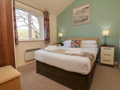 A bedroom with a double bed two bedside tables with lamps a window with floral curtains and a framed picture on the wall at Chalet Log Cabin L2 in Combe Martin