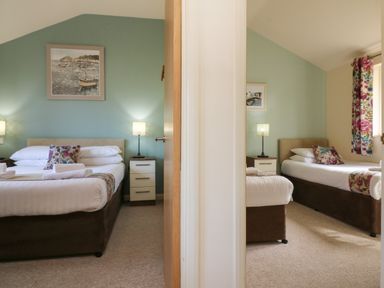 Two bedrooms separated by a wall each with a bed bedside table lamp and wall art at Chalet Log Cabin L2 in Combe Martin