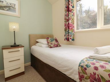 A bedroom with a single bed a nightstand with a lamp and floral curtains at Chalet Log Cabin L2 in Combe Martin