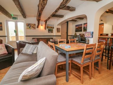 A living area with sofas wooden dining table and chairs under exposed wooden beams at Chalet Log Cabin L2 in Combe Martin