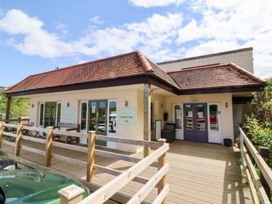 The exterior of a small building with a red tiled roof wooden deck and railing with signs indicating reception and check in at Chalet Log Cabin L2 in Combe Martin