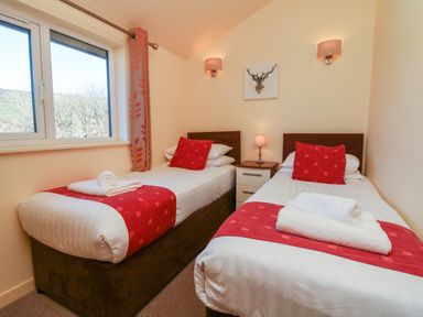 A bedroom with two single beds side by side with red runners and pillows a window and a nightstand with a lamp between beds at Chalet Log Cabin C11 in Combe Martin