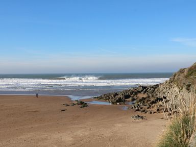 A sandy beach with rocks and people walking near the shore with waves in the ocean at Chalet Log Cabin C11 in Combe Martin