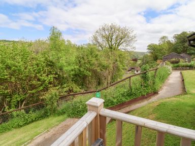 A wooden railing overlooking a pathway with grass and trees at Chalet Log Cabin C11 in Combe Martin