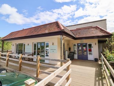 Exterior of a building with wooden deck and railings with signs indicating reception and check in at Chalet Log Cabin C11 in Combe Martin