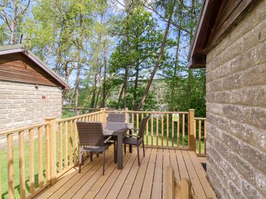 An outdoor wooden deck with a table and four chairs surrounded by trees at Chalet Log Cabin C8 in Combe Martin