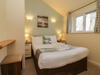 A bedroom with a bed pillows bedside tables lamps and a window at Chalet Log Cabin C9 in Combe Martin