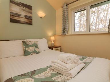 A bedroom with a double bed towels on the bed a window and a bedside table with a lamp at Chalet Log Cabin C9 in Combe Martin