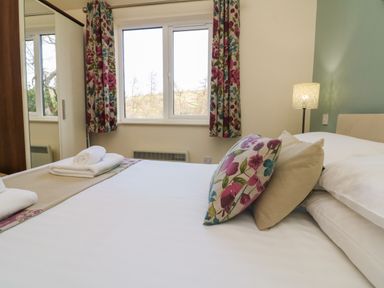 A bedroom with a bed pillows towels floral curtains and a wardrobe at Chalet Log Cabin L3 in Combe Martin
