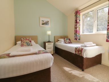 A bedroom with two single beds a nightstand lamp and floral curtains at Chalet Log Cabin L3 in Combe Martin