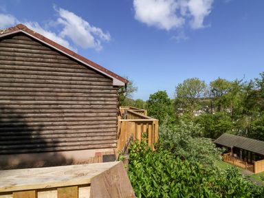 A wooden log cabin with a wooden deck overlooking trees and a nearby cabin at Chalet Log Cabin L3 Combe Martin