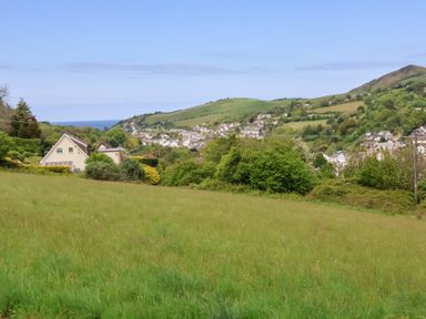 A grassy field with houses and hills in the background at Chalet Log Cabin L3 in Combe Martin
