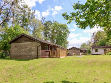 A grassy area with several small cabins surrounded by trees under a partly cloudy sky at Chalet Log Cabin L6 Combe Martin