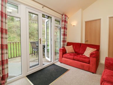 A living room with red sofas beige pillows glass doors opening to a wooden deck with outdoor table and chairs at Chalet Log Cabin L7 Combe Martin
