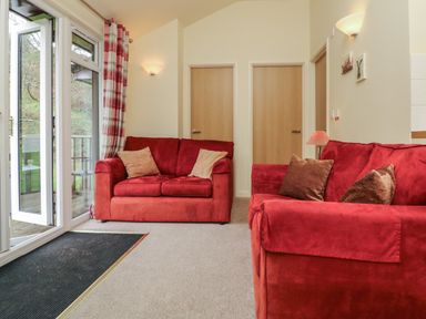 A living room with red sofas and beige pillows near glass doors with red plaid curtains at Chalet Log Cabin L7 in Combe Martin
