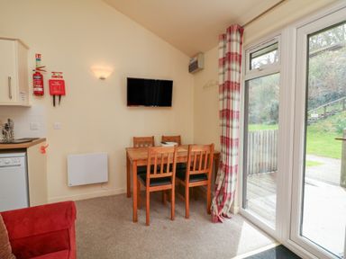 A dining area with a wooden table and four chairs next to glass patio doors with plaid curtains at Chalet Log Cabin L7 in Combe Martin