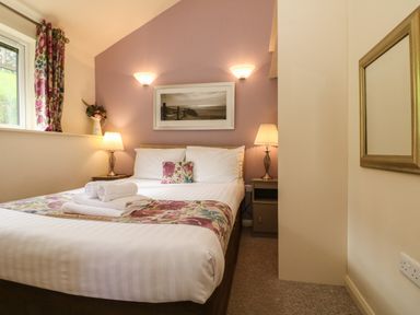 A bedroom with a double bed two bedside tables with lamps a window with floral curtains and a framed picture on the wall at Chalet Log Cabin L10 in Combe Martin