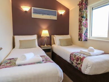 A bedroom with two single beds a nightstand with a lamp and a window with floral curtains at Chalet Log Cabin L10 in Combe Martin