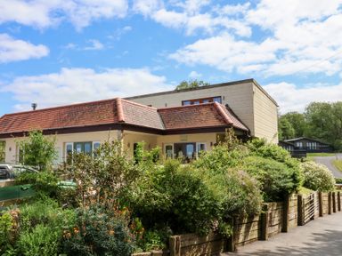 A building with a red tiled roof and garden in front surrounded by wooden fencing at Chalet Log Cabin L10 in Combe Martin