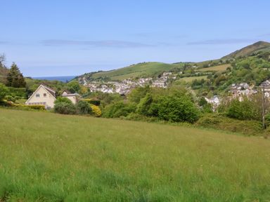 A grassy field with houses and trees in the distance and hills in the background at Chalet Log Cabin L10 Combe Martin