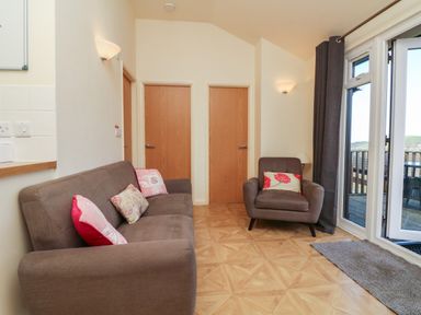 A seating area with a sofa and armchair with cushions near two wooden doors and glass doors leading to a balcony at Chalet Log Cabin L12 in Combe Martin